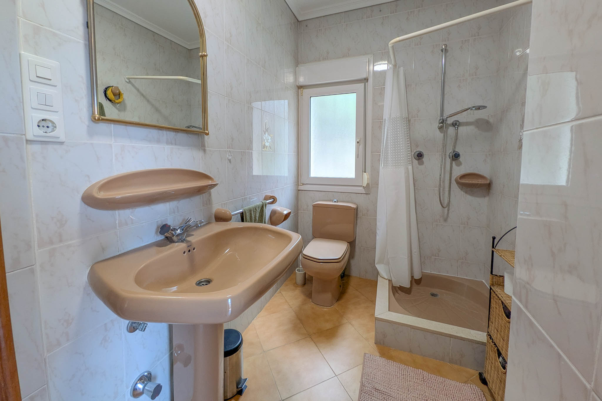 Badkamer met beige sanitair, een douche met gordijn, volledig betegelde wanden en een raam voor natuurlijke lichtinval.