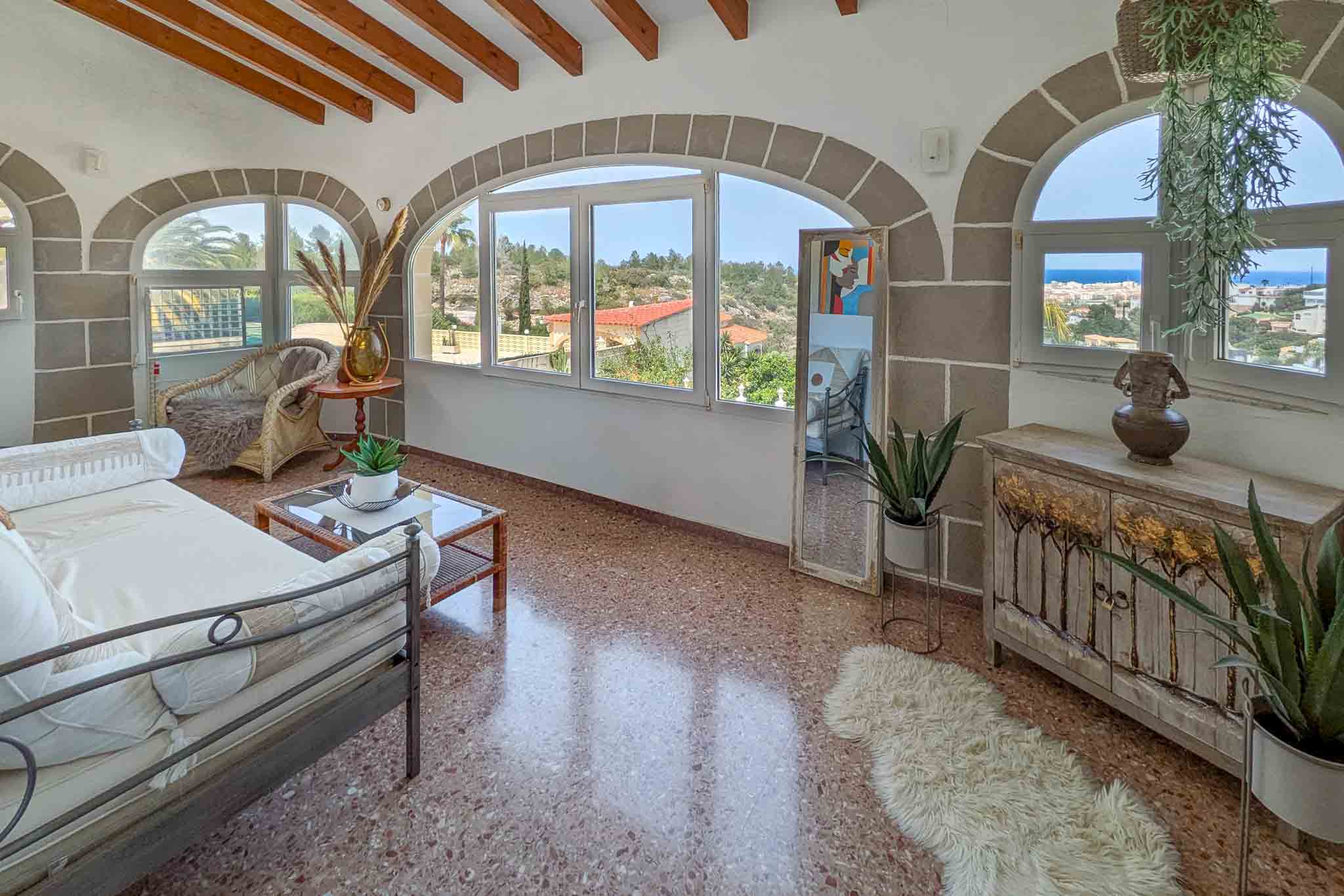 Beglaasd terras met stenen bogen, houten balkenplafond en terrazzovloer. De grote raampartijen bieden panoramisch uitzicht op de Middellandse Zee en Dénia.