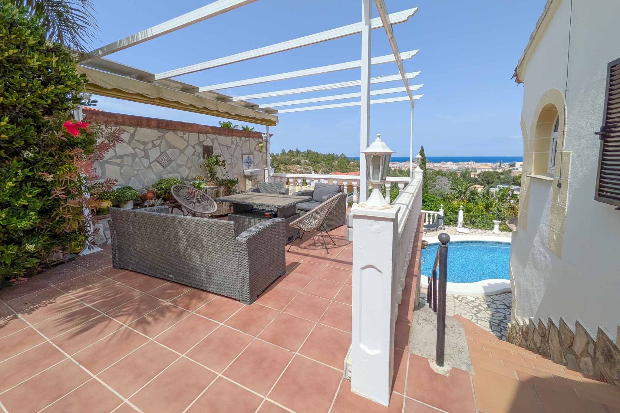 Bovenste terras met buitenlounge, witte pergola en panoramisch uitzicht op de Middellandse Zee en Dénia, uitkijkend over het zwembad.
