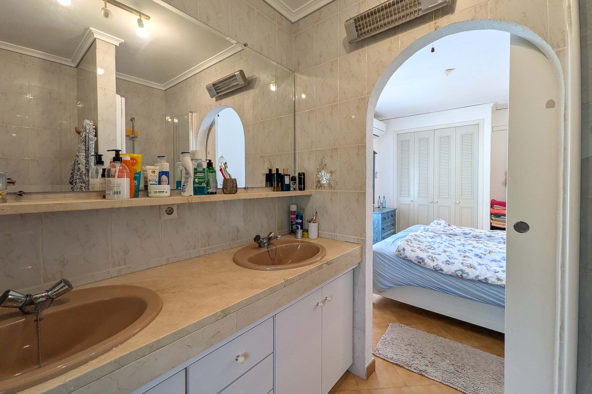 En-suite badkamer met dubbele wastafel op een marmeren blad, verbonden met de slaapkamer via een karakteristieke boogingang.