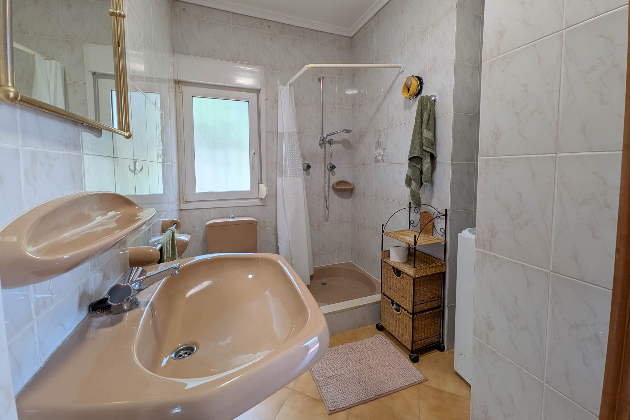 Functionele badkamer met zalmkleurig sanitair, douchebak met gordijn, betegelde wanden en een raam voor natuurlijke ventilatie.