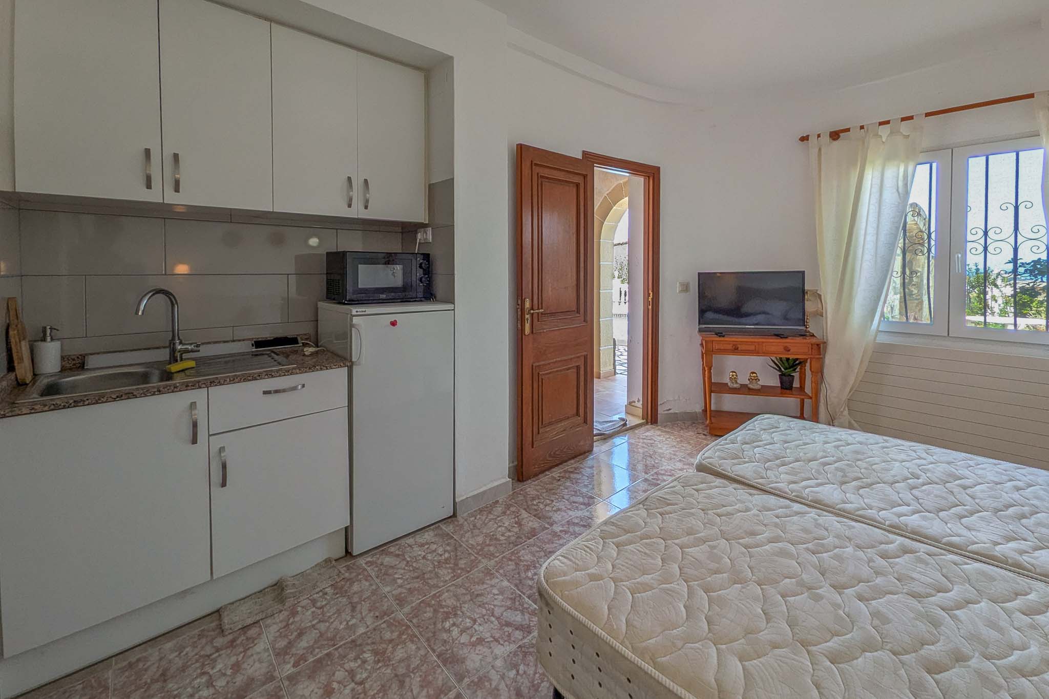 Onafhankelijk appartement op de begane grond met een compacte kitchenette, twee eenpersoonsbedden en directe toegang tot het terras via een houten deur.