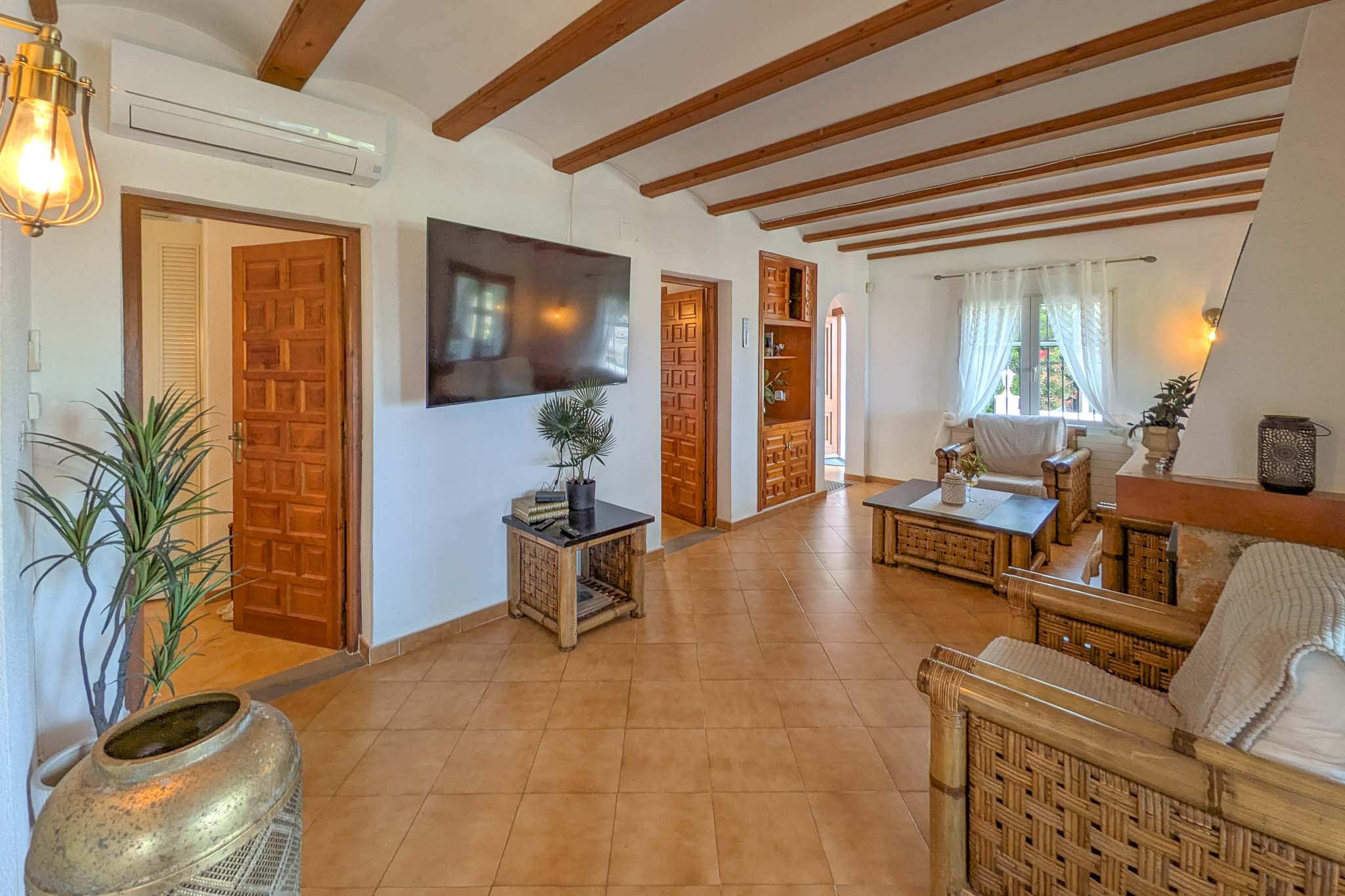 Rustieke woonkamer met zichtbare houten balken, terracotta vloertegels en bamboe meubilair. Voorzien van airconditioning en decoratieve houten deuren.