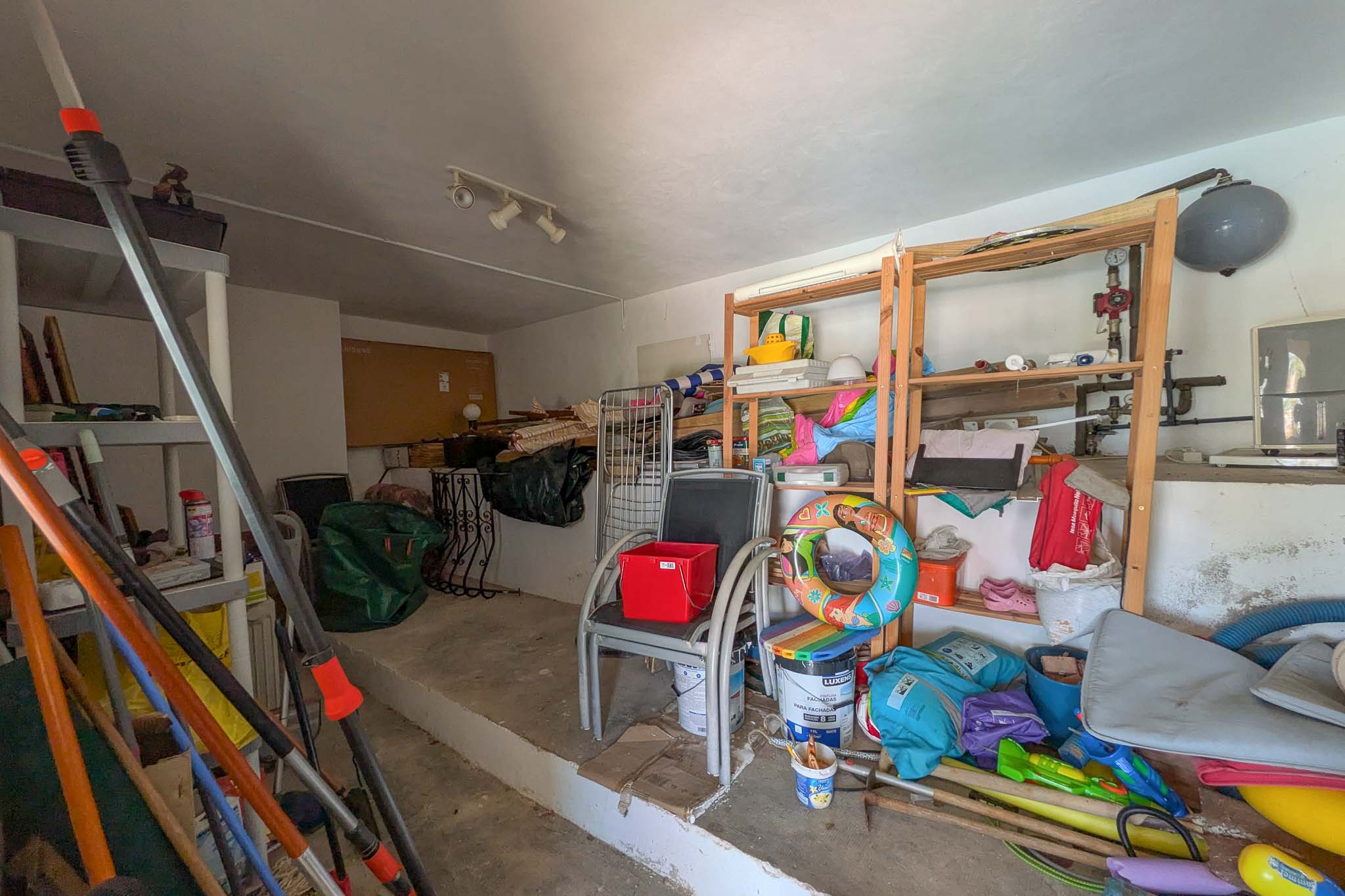 Veelzijdige bergruimte met betonnen vloer en houten stellingen, geschikt voor het opslaan van huishoudelijke artikelen en tuinbenodigdheden.