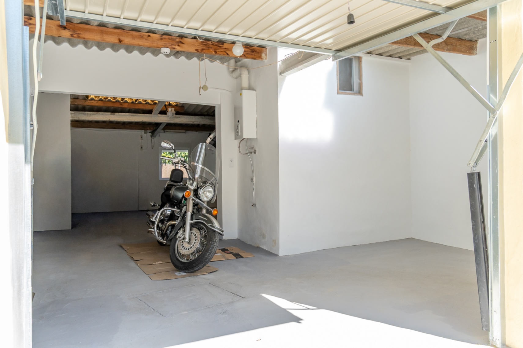 Afgesloten garage en parkeerplaats met betonvloer, houten plafondbalken en een wandgemonteerde gasboiler, geschikt voor voertuigen en opslag.