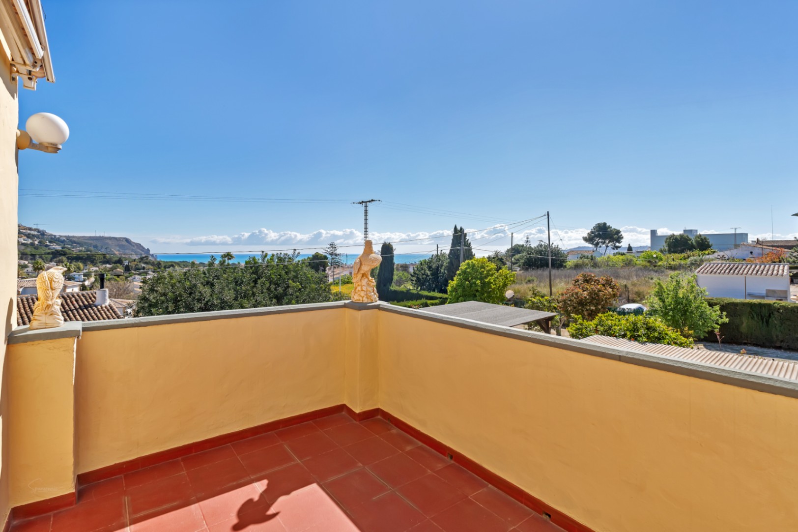 Bovenste terras met terracotta tegels en gele muren, met een weids panoramisch uitzicht over de Middellandse Zee en de omliggende kustlijn van Jávea.