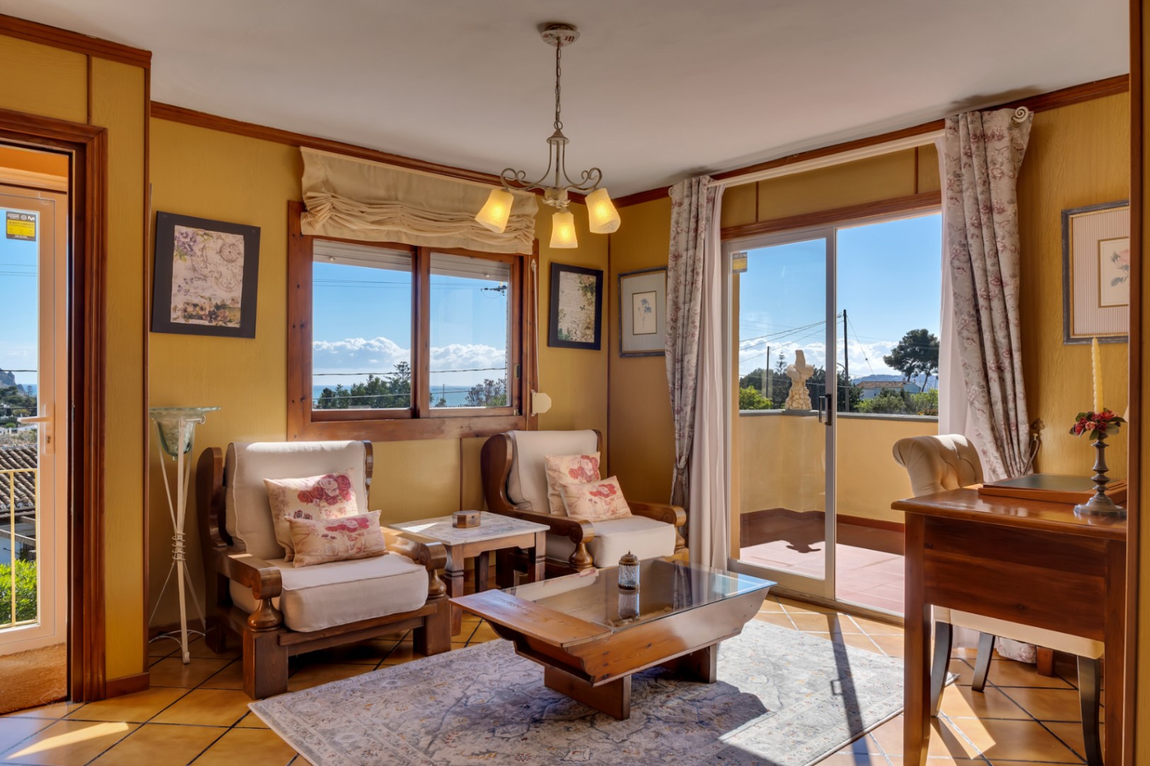 Lichte woonkamer met houten fauteuils, glazen salontafel en schuifpui naar het terras met panoramisch uitzicht op de Middellandse Zee.