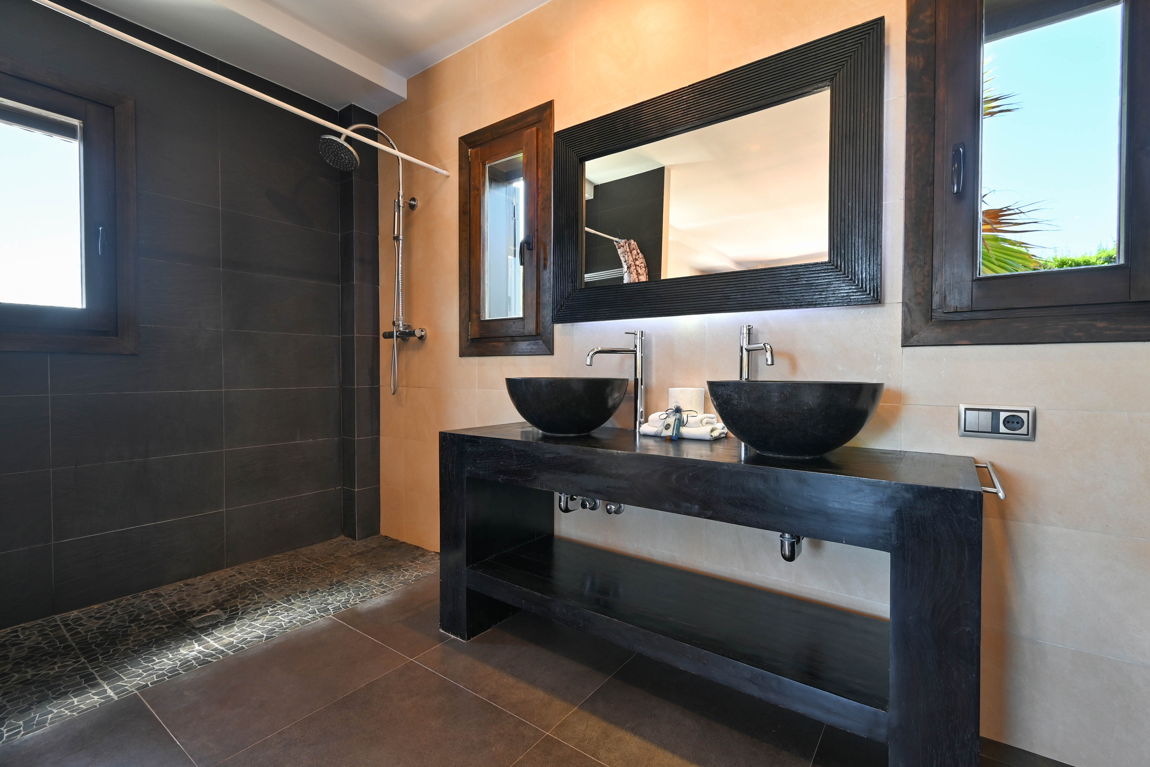 Detail van een moderne badkamer met dubbele stenen wastafel en donkere betegelde douche.