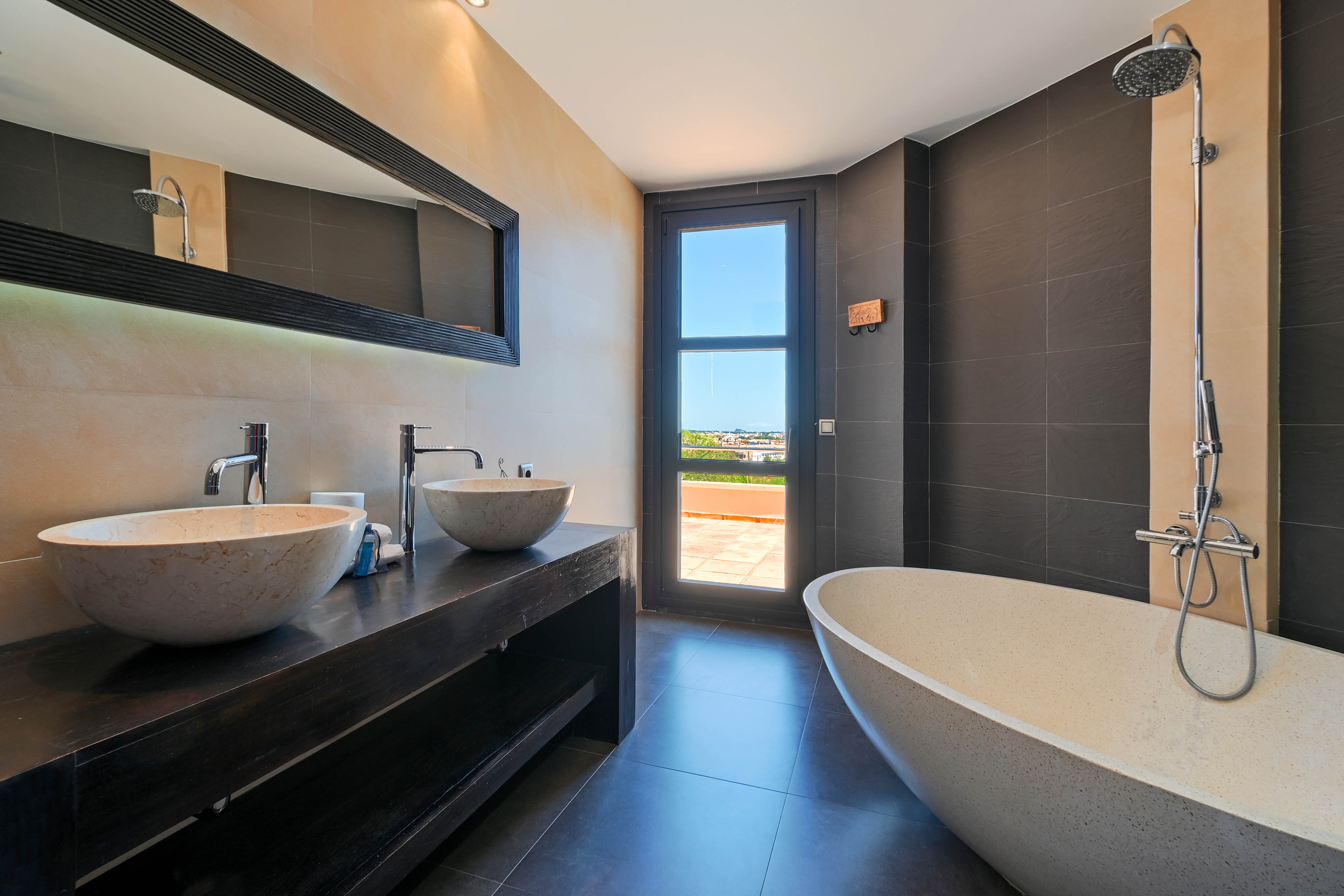 Elegante badkamer met dubbele stenen wastafels en een vrijstaand bad, met toegang tot een buitenterras.