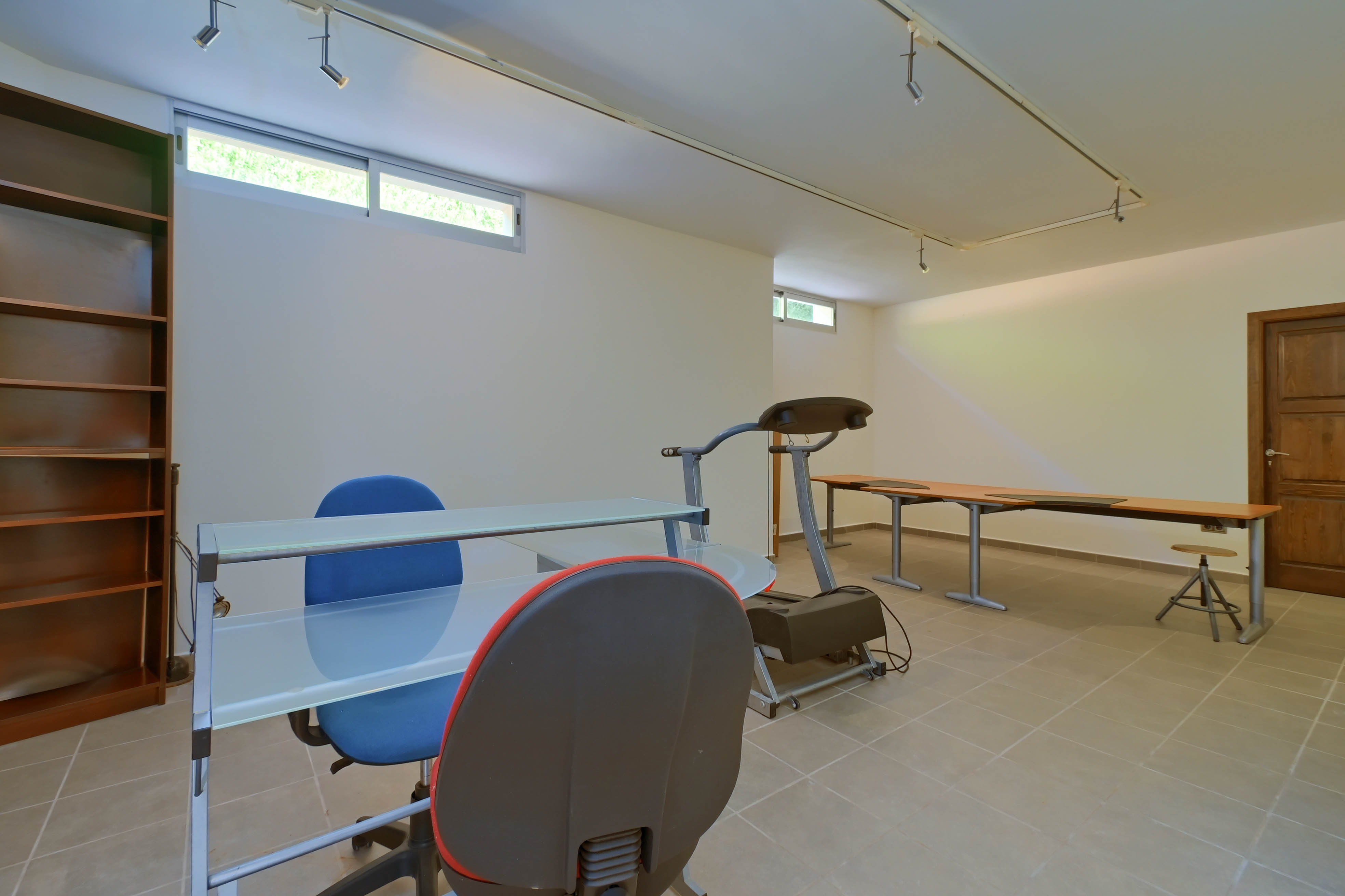 Functionele ruimte met stellingkast, glazen bureau en loopband op neutrale tegelvloer.