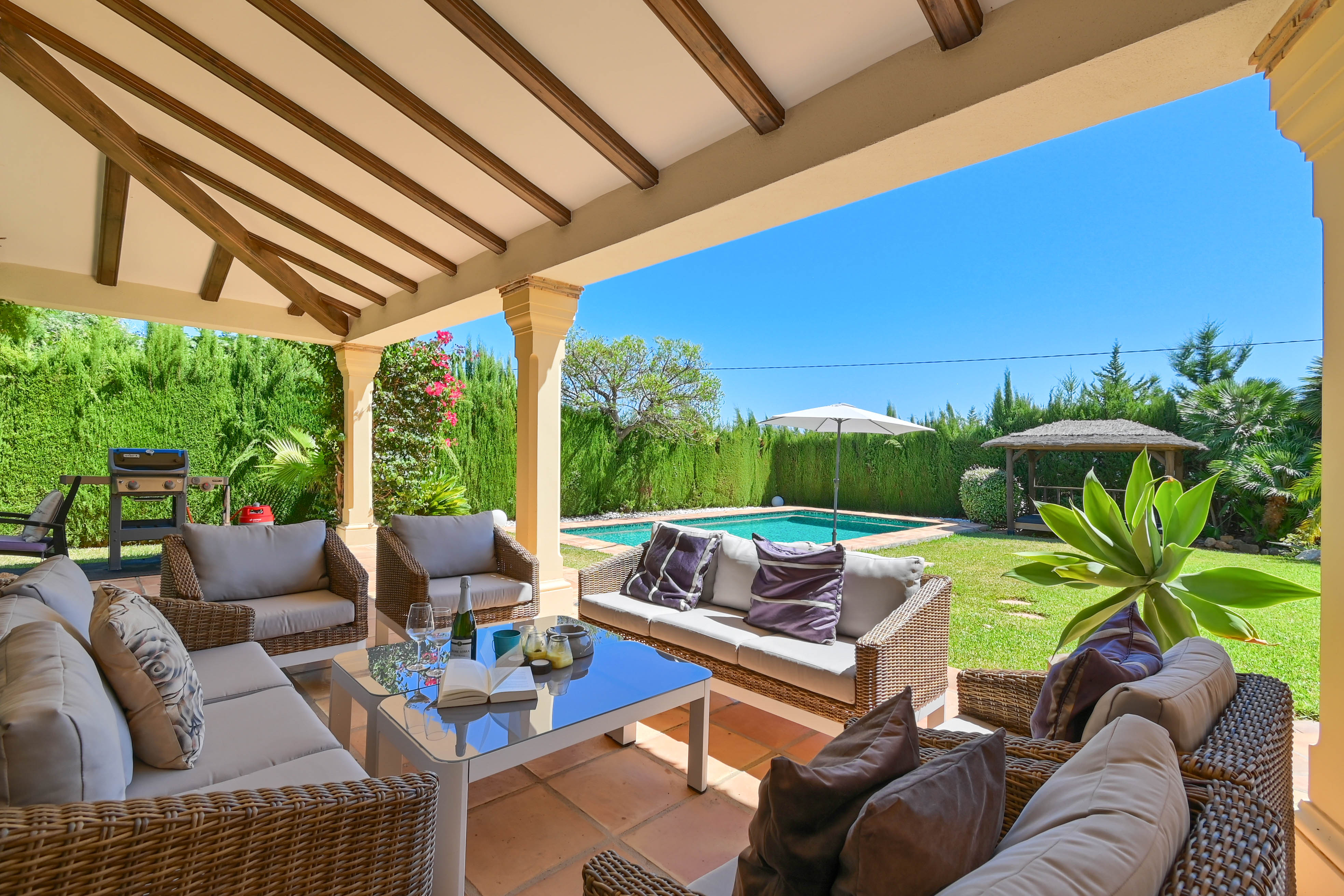 Gemeubileerde veranda met rieten banken met uitzicht op het zwembad en de tuin.