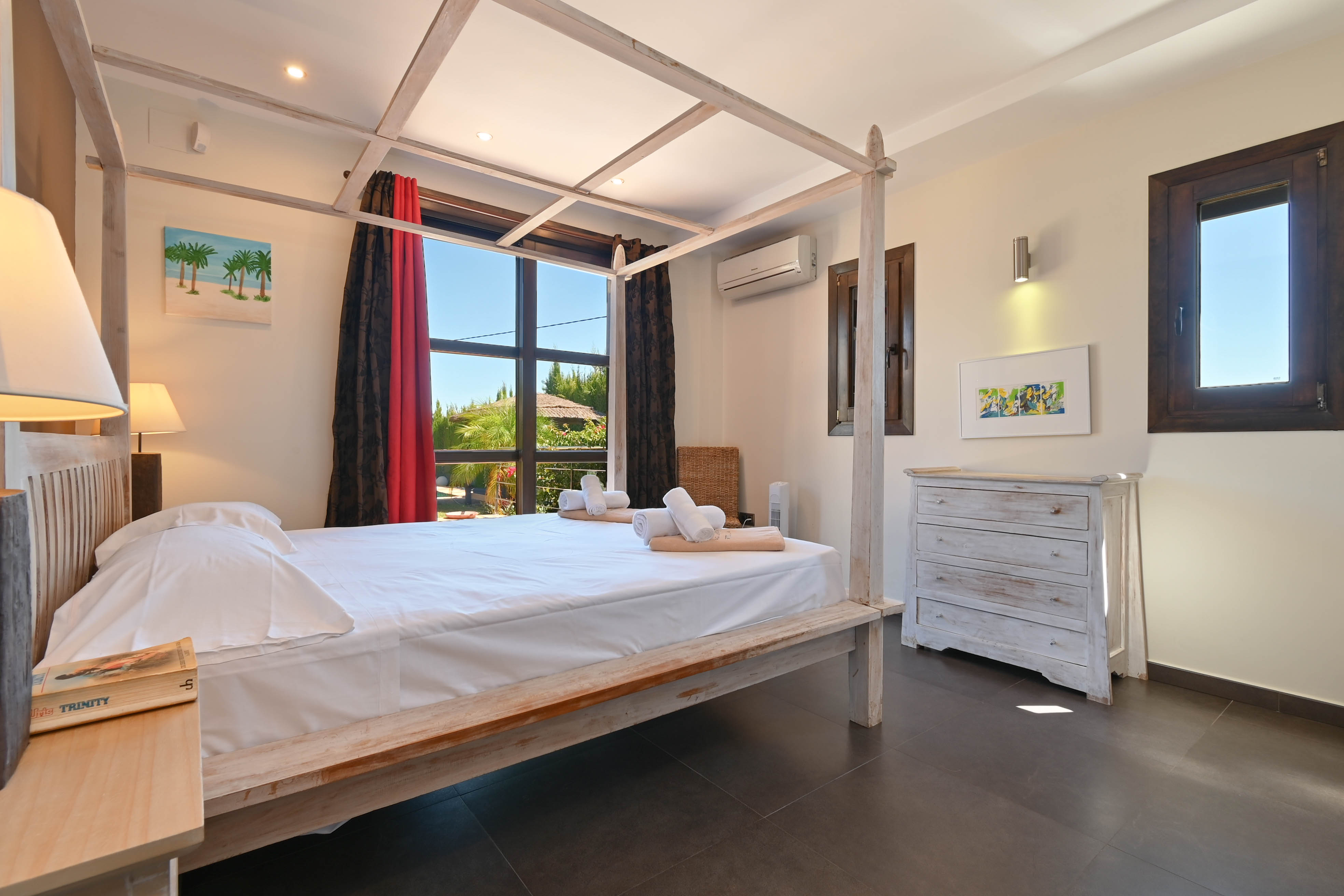Lichte slaapkamer met een licht houten hemelbed en een witte commode in brocante stijl.