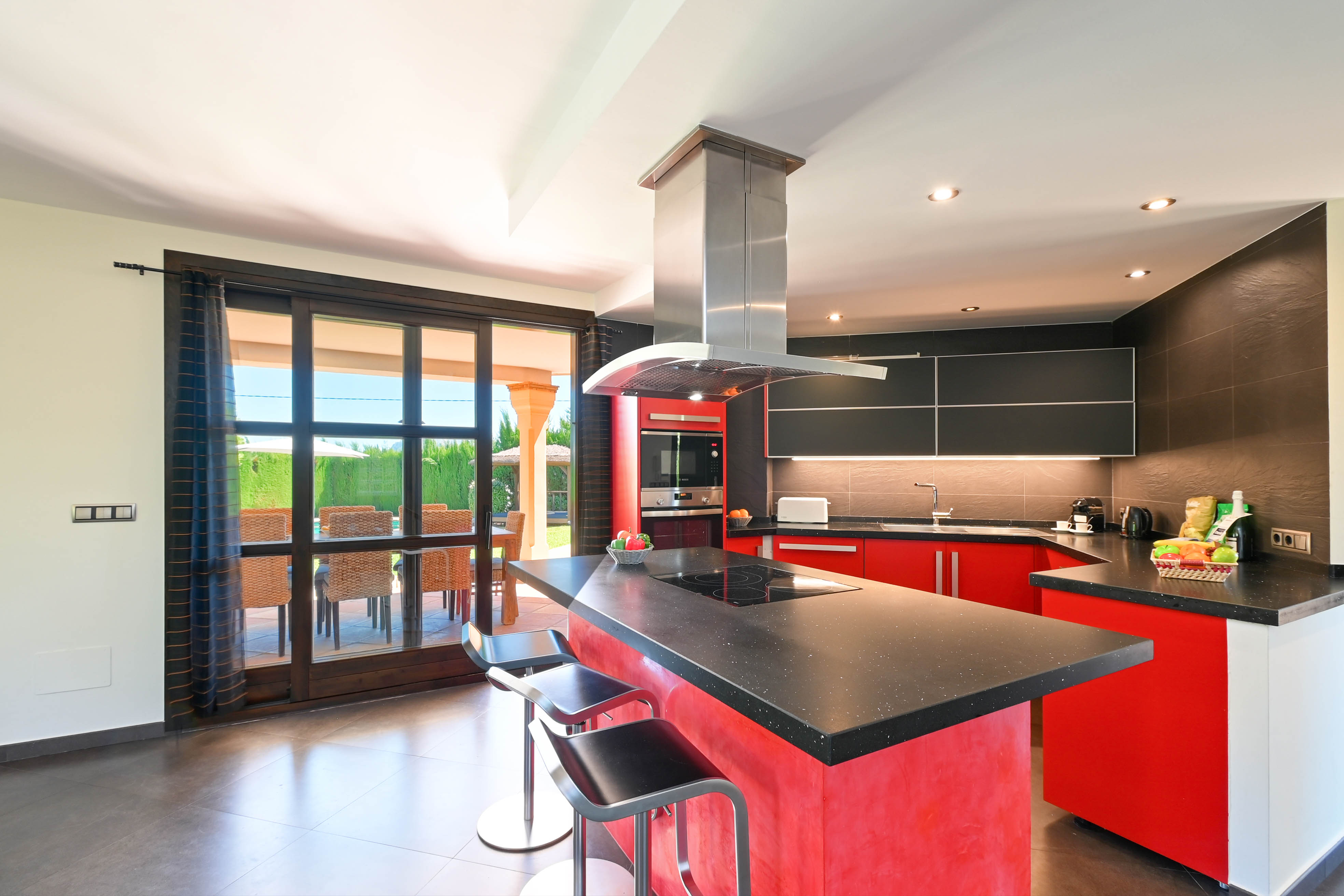 Moderne keuken met centraal eiland, zwart granieten aanrechtblad en metalen krukken.