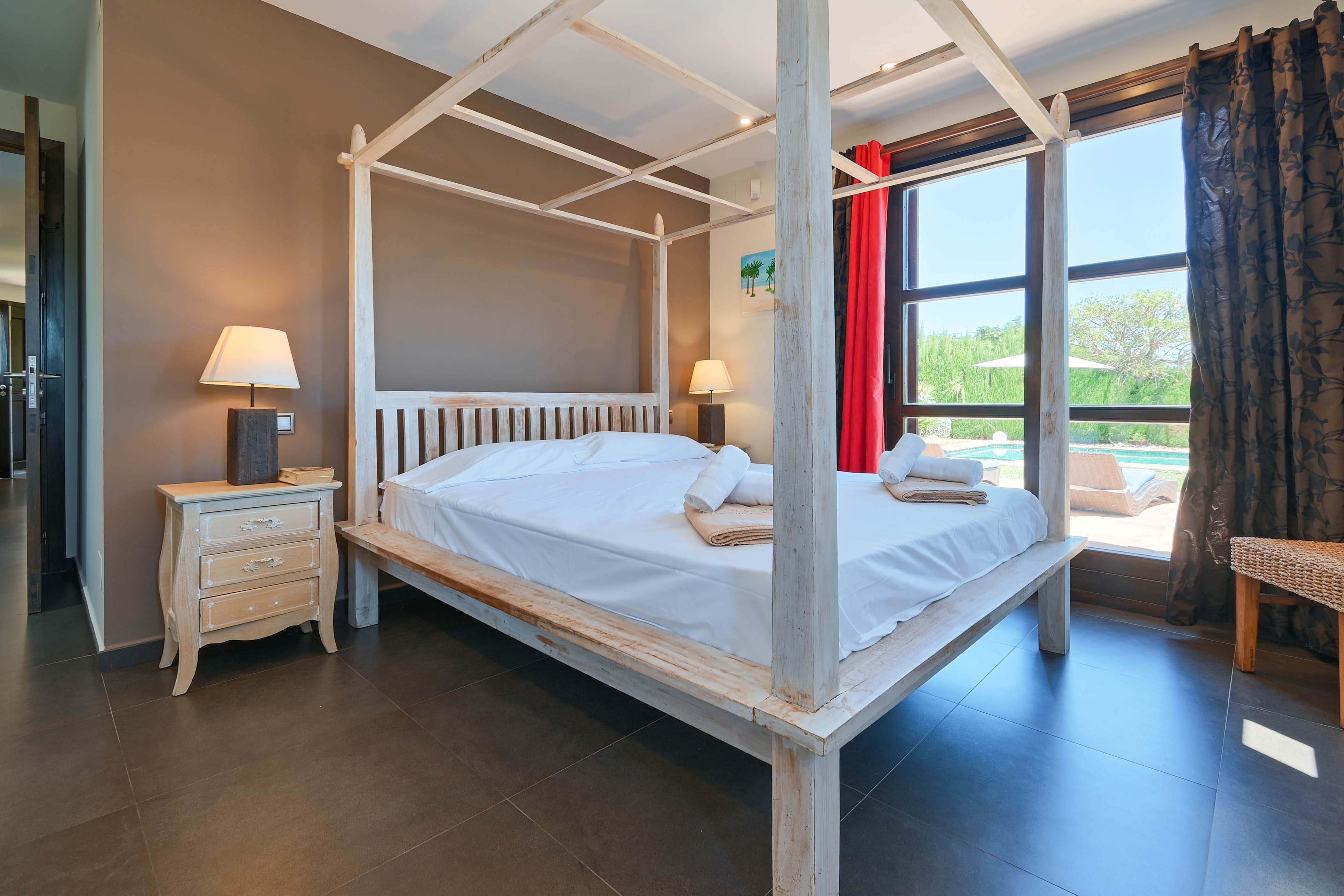Slaapkamer met wit houten hemelbed, nachtkastje in brocante stijl en uitzicht op het zwembad.