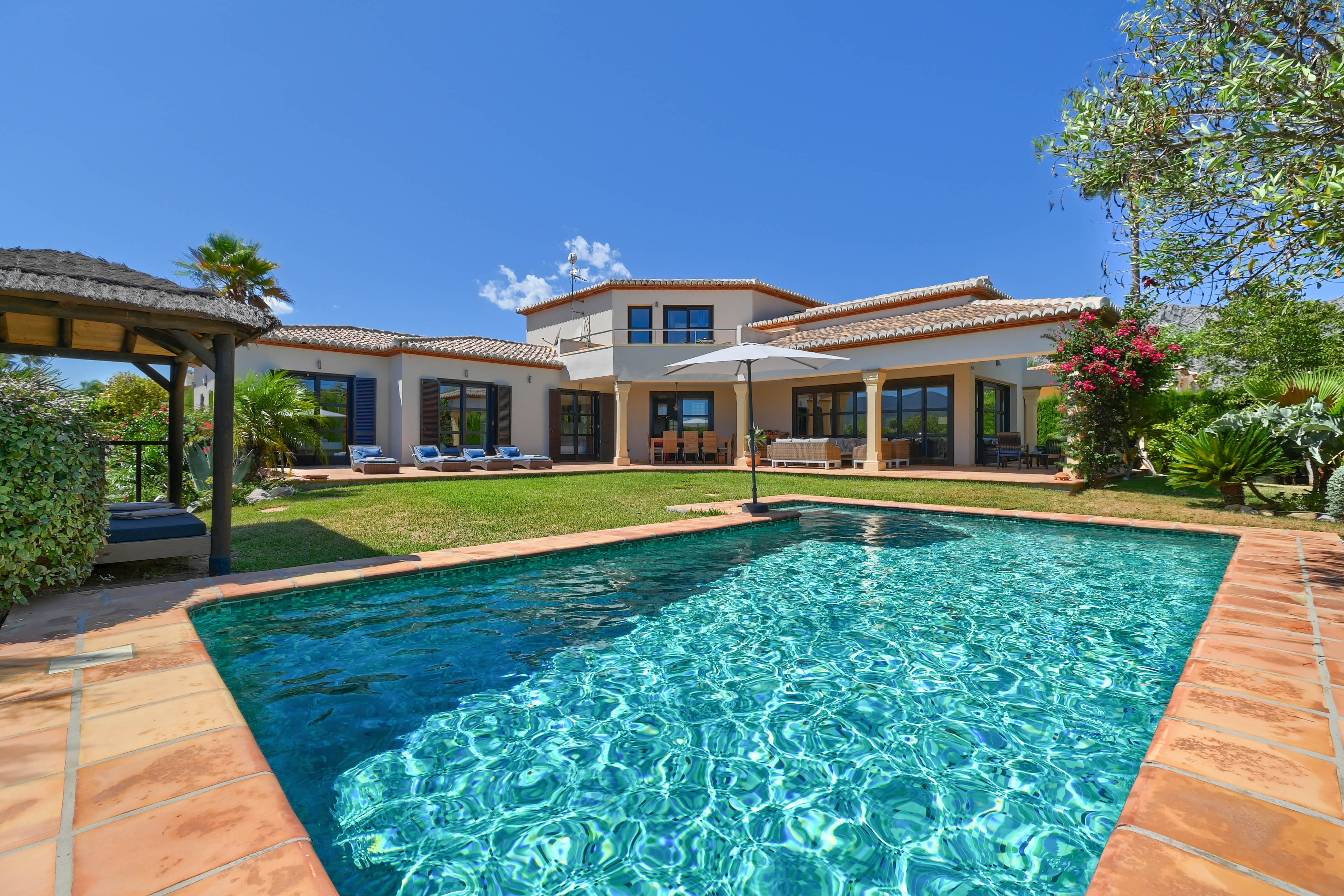Uitzicht op het turquoise zwembad met terracotta rand en de villa met twee verdiepingen en luiken.