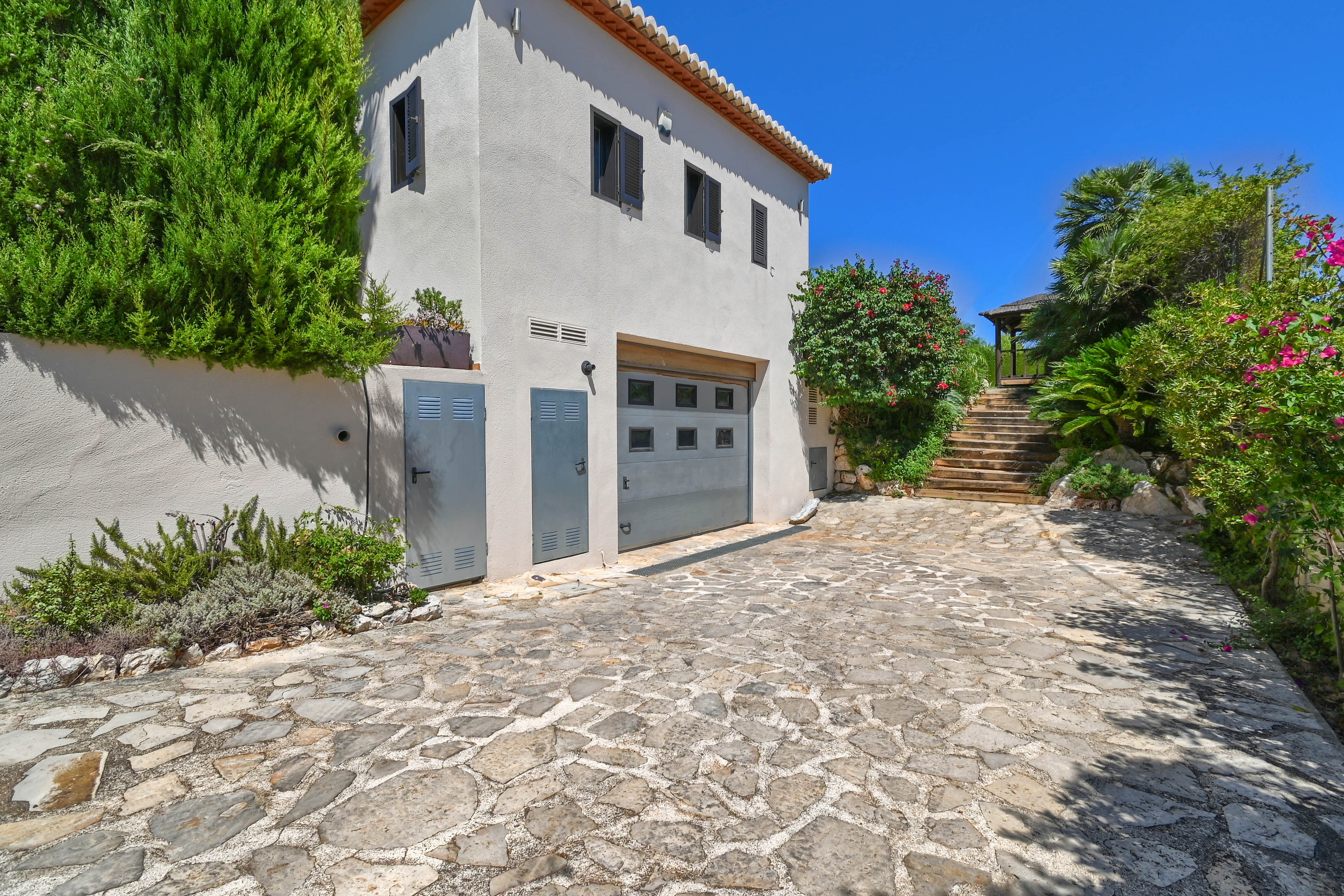 Villa-exterieur met stenen oprit, groen en een grijze garage.