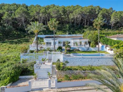 Buitenaanzicht van de villa in Piver, Jávea, met witte gevel, zwembad en terrastuinen met mediterrane begroeiing.