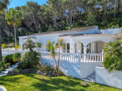 Buitenaanzicht van de villa met overdekt terras, balustrade en tuin met mediterrane begroeiing.