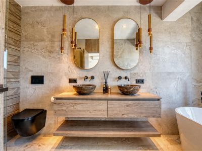 Elegante badkamer met stenen waskommen, zwevend houten wastafelmeubel en gouden hanglampen. Modern design met neutrale tegels.