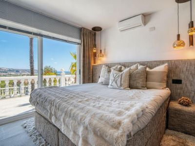 Lichte slaapkamer met toegang tot terras en uitzicht op zee. Bed met gestoffeerd hoofdeinde en beddengoed in neutrale tinten.