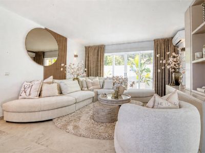 Lichte woonkamer met beige modulaire bank, zacht vloerkleed en decoratieve ronde spiegel.