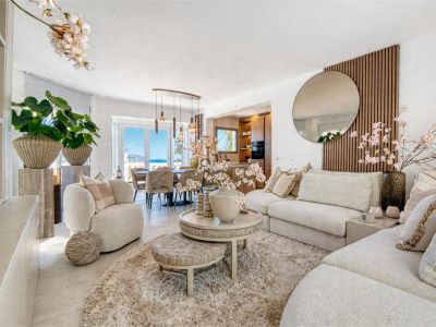 Lichte woonkamer met neutrale inrichting, zacht vloerkleed en toegang tot de eetkamer met zeezicht.