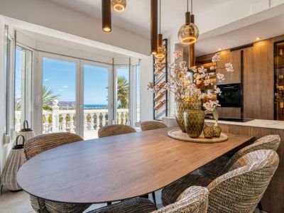 Moderne eetkamer met houten tafel, gestoffeerde stoelen en uitzicht op de Middellandse Zee door grote ramen.