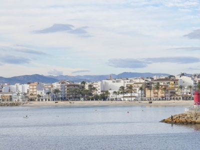Panoramisch uitzicht op het strand en de boulevard van Jávea, met woongebouwen en bergen op de achtergrond.