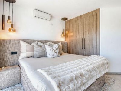 Slaapkamer met gestoffeerd hoofdeinde, design hanglampen en een ingebouwde kledingkast van licht hout.