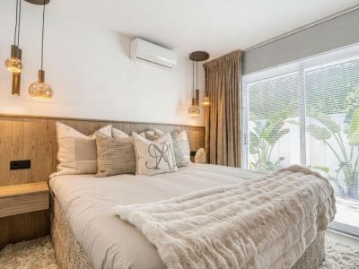 Slaapkamer met houten hoofdeinde, glazen hanglampen en beige gordijnen naast een raam.