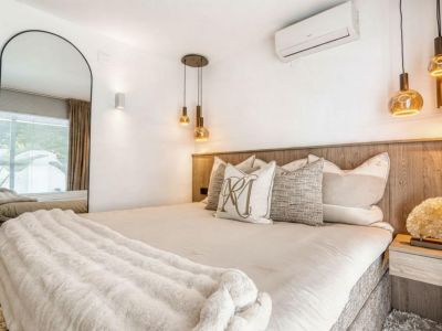 Slaapkamer met houten hoofdeinde, gouden hanglampen en een spiegel over de volledige lengte.