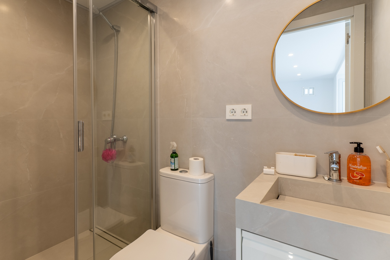 Badkamerdetail met glazen douche, moderne wastafel en ronde spiegel met gouden frame.