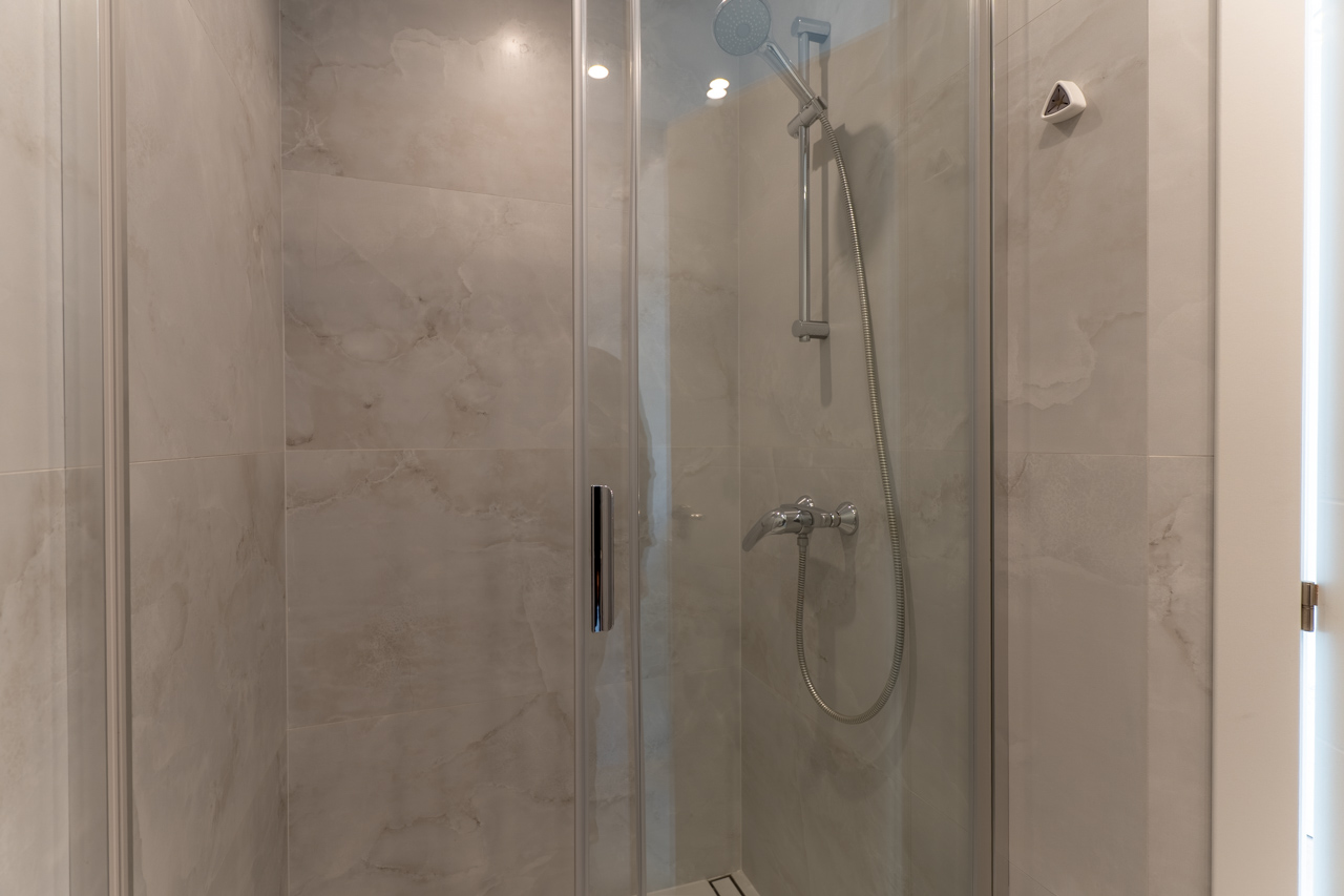 Detail van de douche met glazen scherm en keramische tegels met marmerlook.