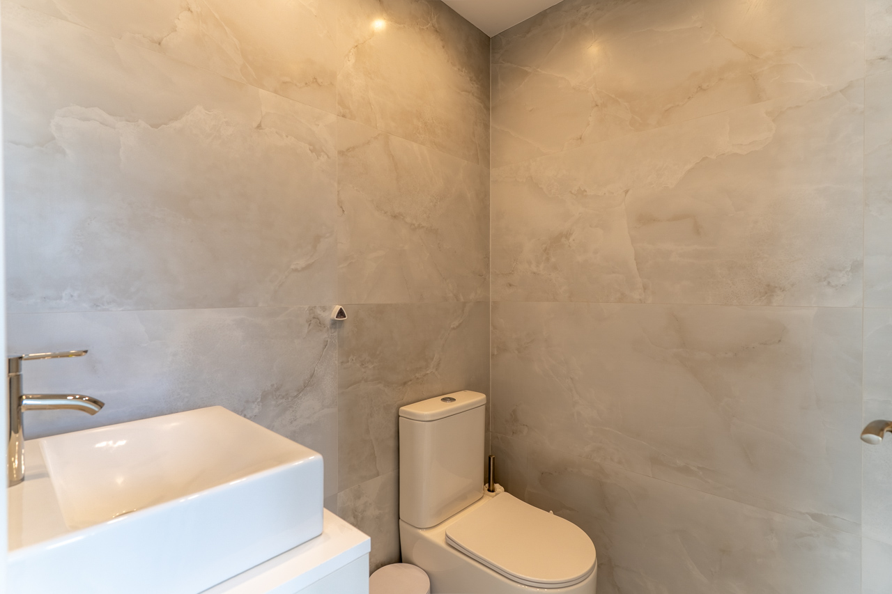 Detail van moderne badkamer met geaderde tegels, vierkante wastafel op wit blad en modern toilet.