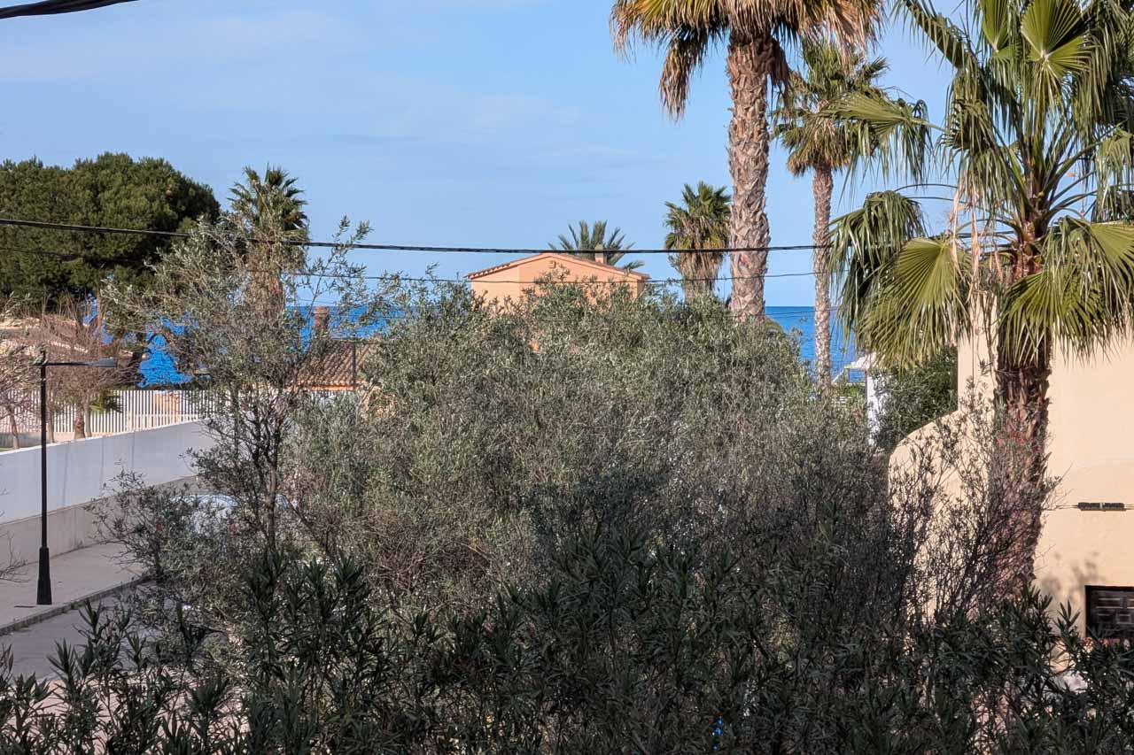 Gedeeltelijk zicht op het pand met mediterrane vegetatie en de zee op de achtergrond.
