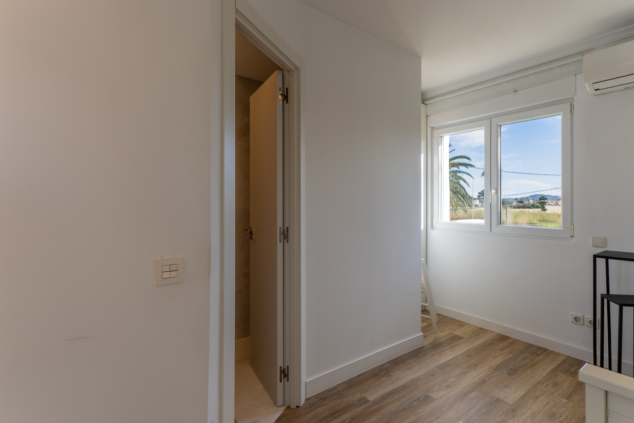 Lichte kamer met houtlook vloer en uitzicht naar buiten. Deur op een kier naar de badkamer.