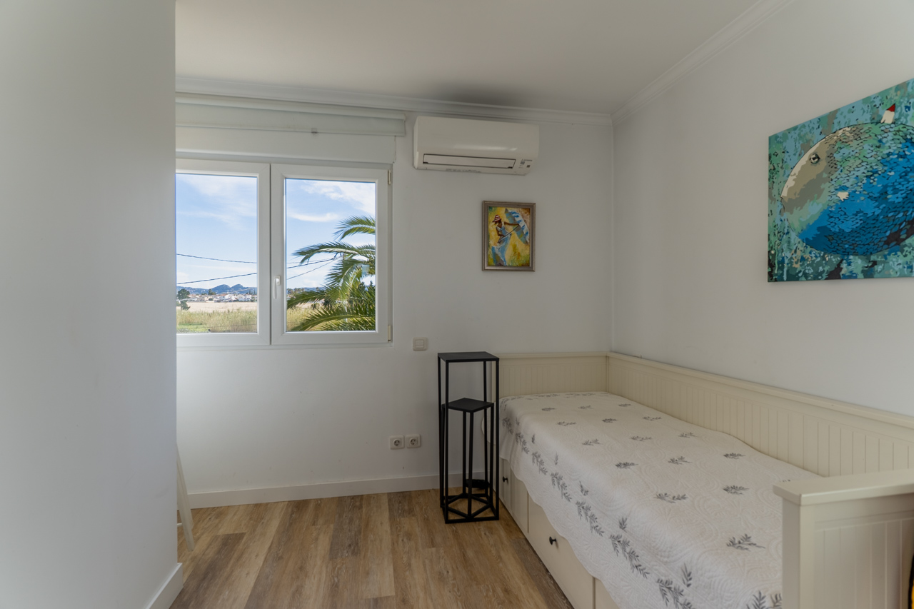 Lichte slaapkamer met eenpersoonsbed, moderne inrichting en uitzicht op de buitenkant met palmbomen.