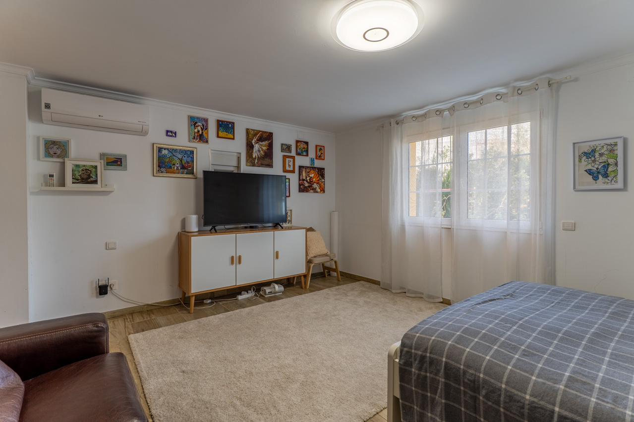 Lichte slaapkamer met zacht vloerkleed, wit tv-meubel en eclectische kunst aan de muur.