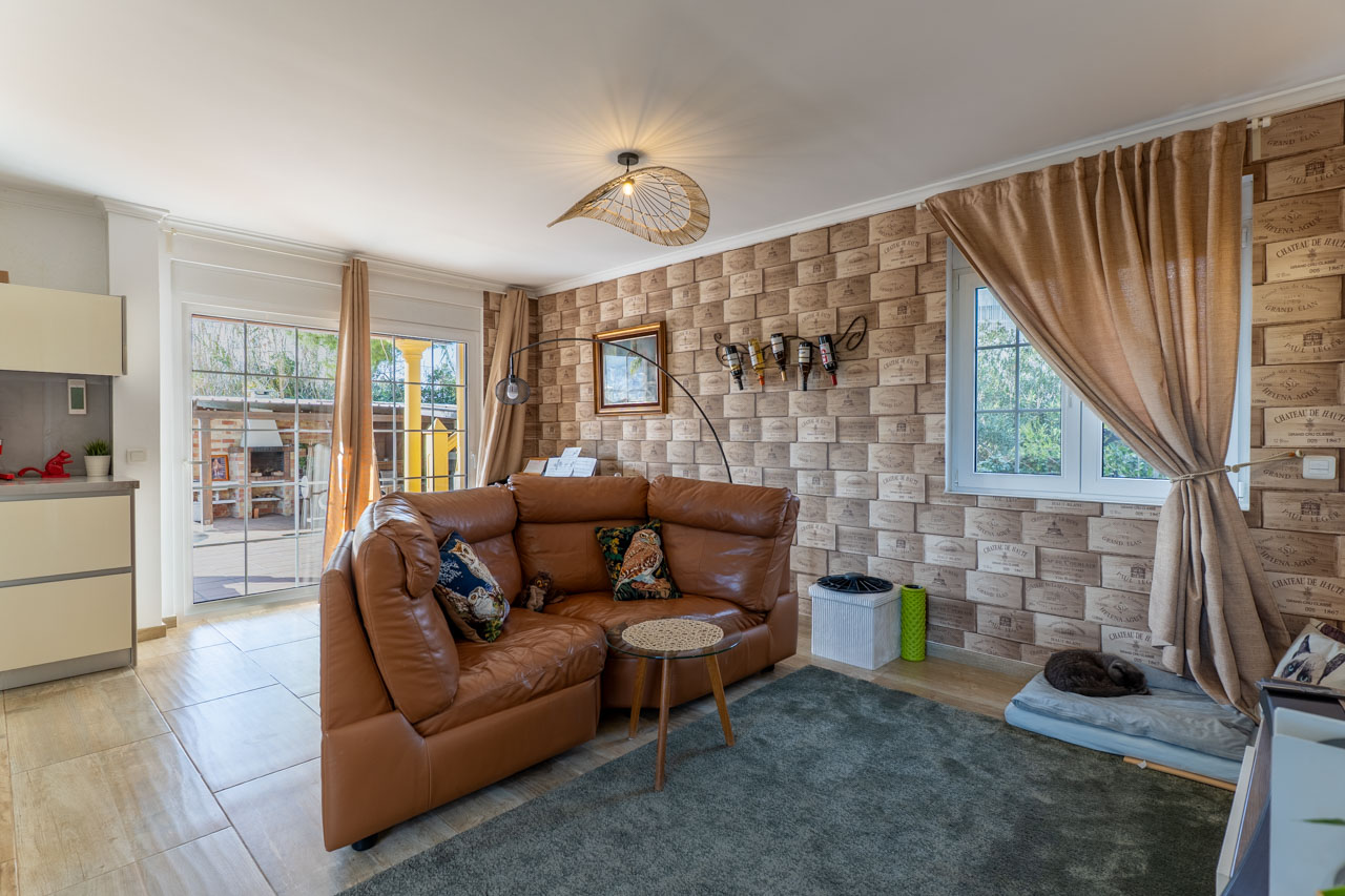 Lichte woonkamer met leren bank, behang met wijnkratmotief en toegang tot het terras.