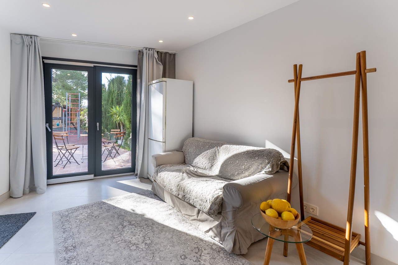 Lichte woonkamer met overdekte bank, toegang tot de patio en minimalistische inrichting.
