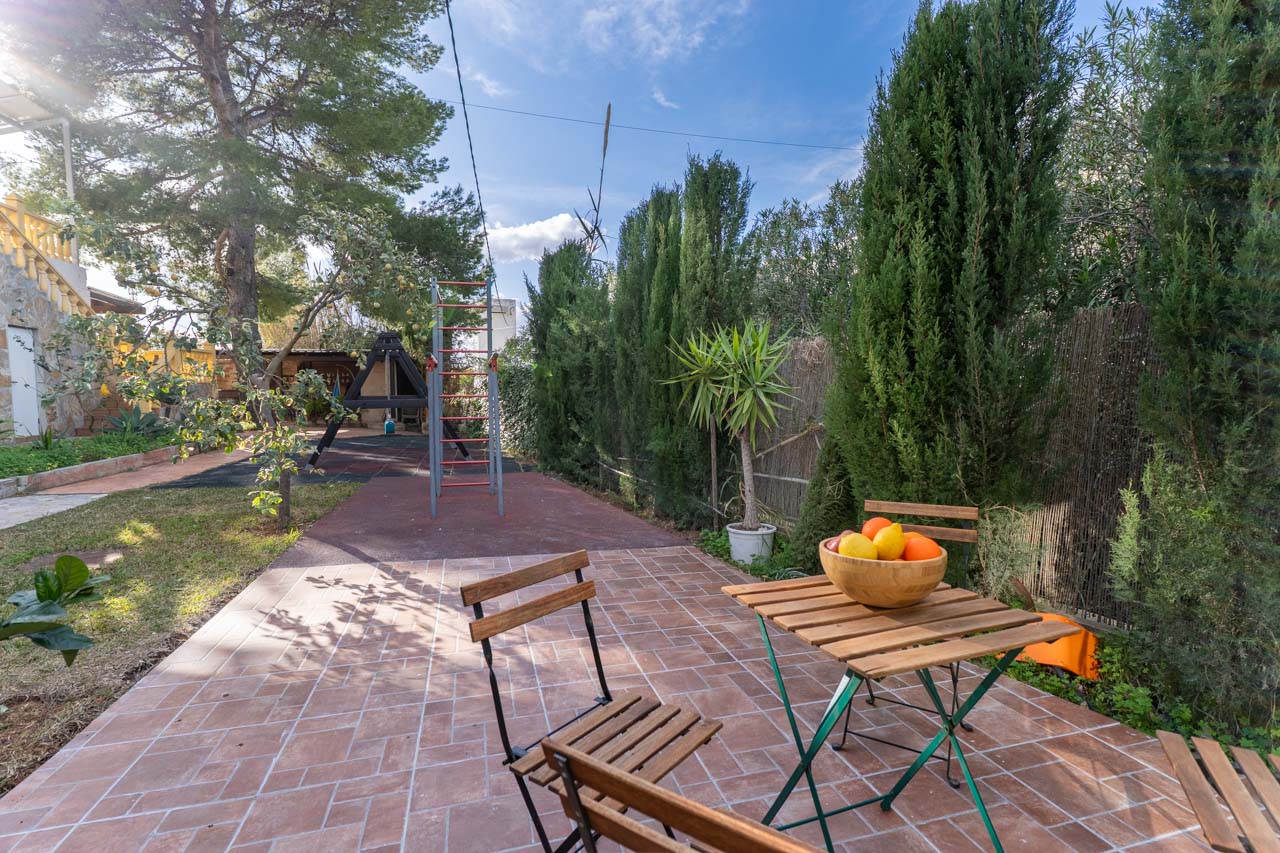 Terras met houten tafel en fruitschaal, omgeven door groen en een kinderspeelplaats.