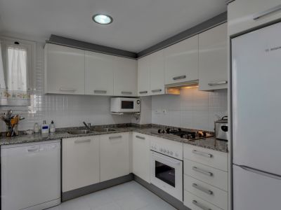 Functionele keuken met granieten aanrechtblad, witte apparaten en bovenlicht.