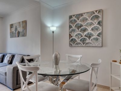 Lichte eetkamer met een ronde glazen tafel en witte stoelen, aangevuld met moderne kunst en een staande lamp.