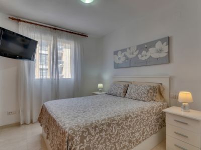 Lichte slaapkamer met tweepersoonsbed, witte nachtkastjes en tv aan de muur.