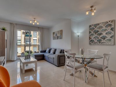 Lichte woon-eetkamer met glazen tafel, grijze hoekbank en toegang tot het balkon met uitzicht op de stad.