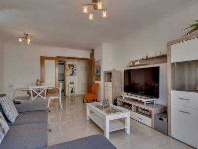 Lichte woonkamer met tegelvloeren, een grijze bank en moderne meubels in neutrale en witte tinten.