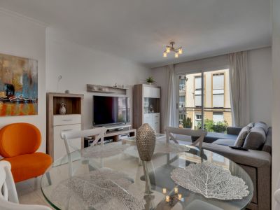 Woon-eetkamer met glazen tafel, witte stoelen en een grijze bank, verlicht door natuurlijk licht.