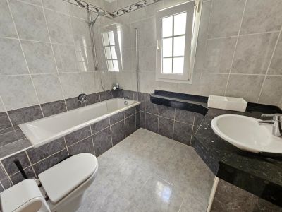 Badkamer met grijze tegels, een ligbad met glazen scherm en een zwart granieten aanrecht.