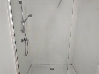 Detail van de douche met glazen wand en stalen armaturen in een moderne badkamer.