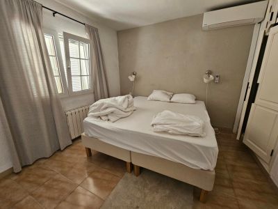 Slaapkamer met tweepersoonsbed, linnen gordijnen en rustieke tegelvloer.